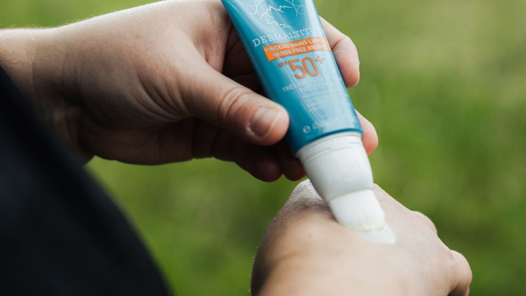 Application de crème solaire indice 50+ sur la main à l’aide d’un tube avec pinceau applicateur.